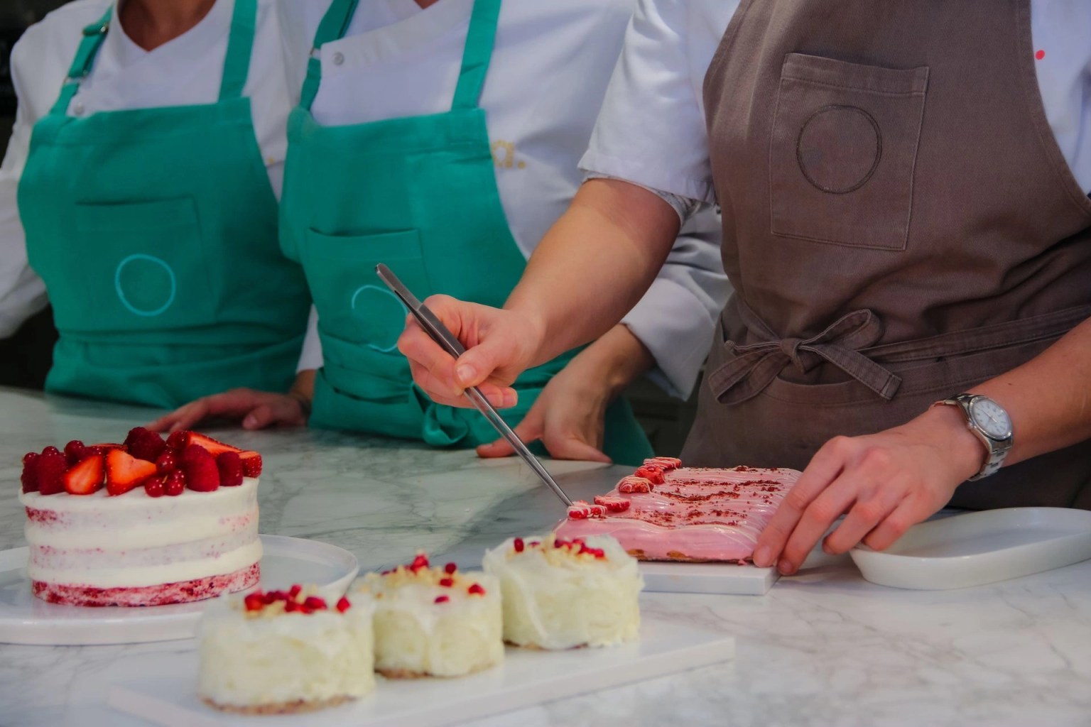 Personas preparando y decorando pasteles en una cocina de repostería, imagen para una guía sobre cómo crear un negocio de repostería en casa.