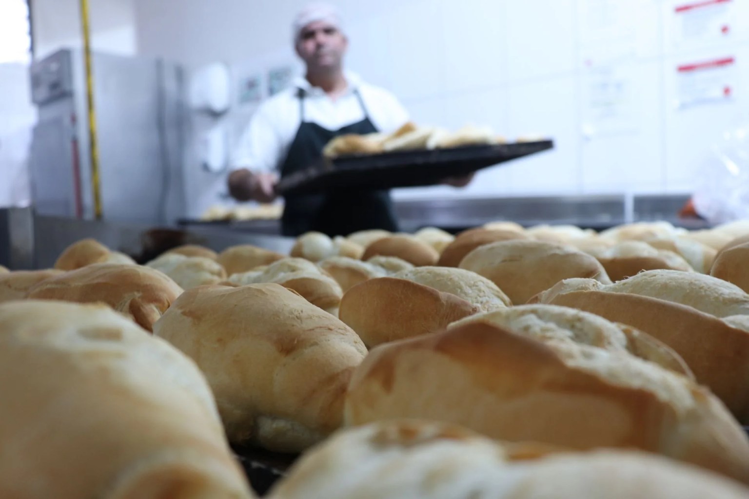 Panes recién horneados en una panadería con un panadero trabajando al fondo